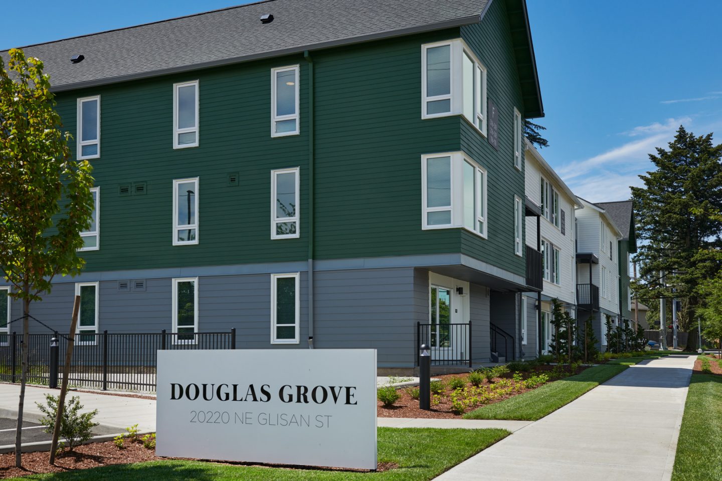 A Granite Sign Reading Douglas Grove Apartments Sits In Front Of The Green And Grey Building.
