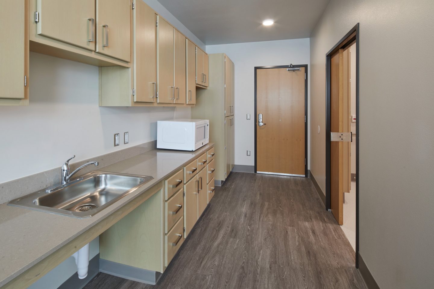 A Wide Entry Hallway Is Flanked By A Kitchenette With Wood Cabinets.