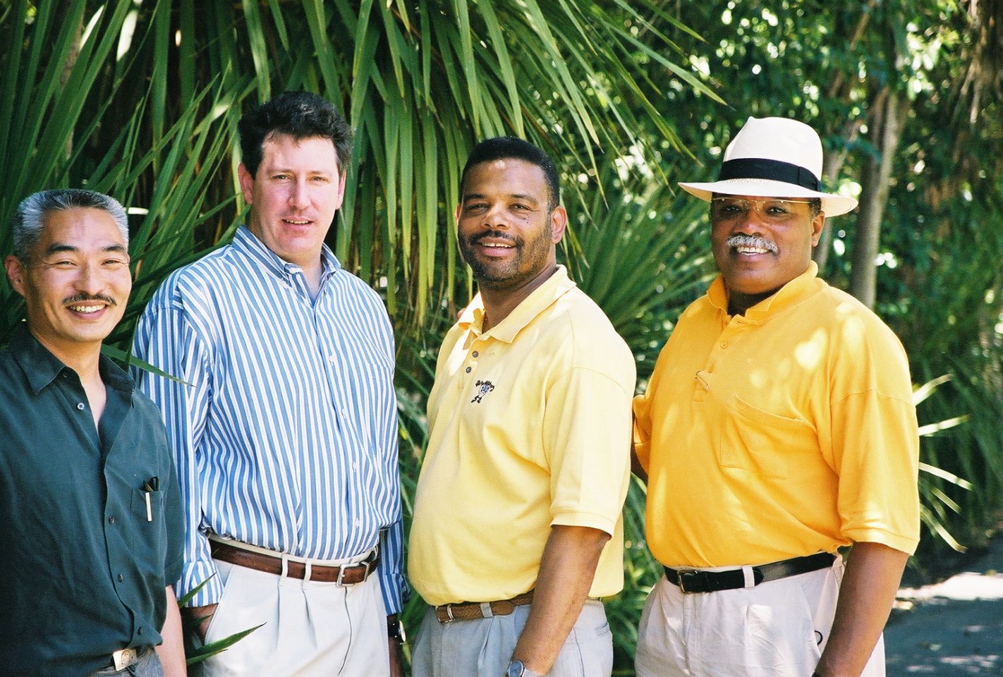 Four MWA Principals standing in front of palm trees. Photo represents MWA's diversity in leadership with one Asian principal, two Black principals, and one Caucasian principal.