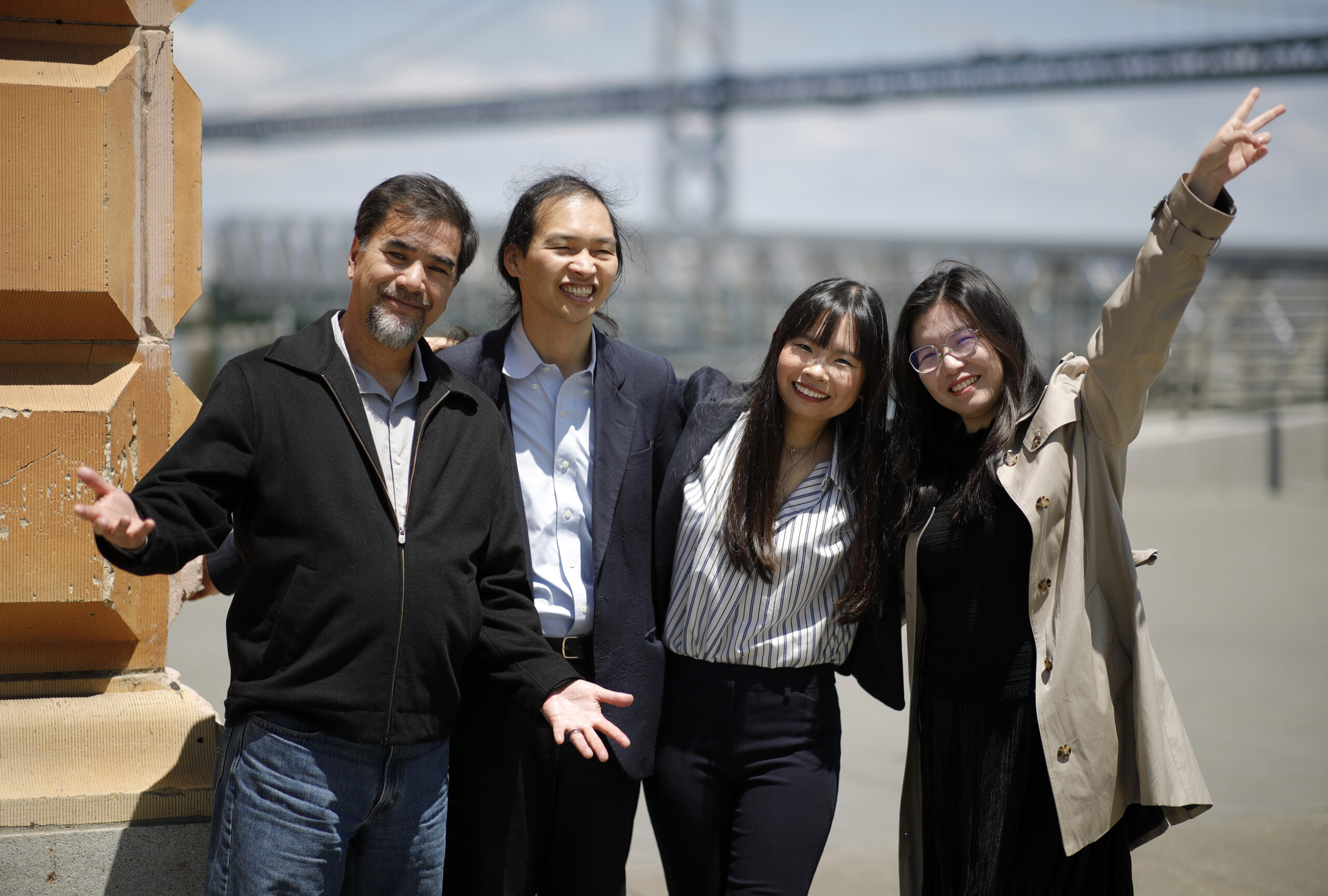 Four people wearing business clothes standing in front of the Bay Bridge smiling.
